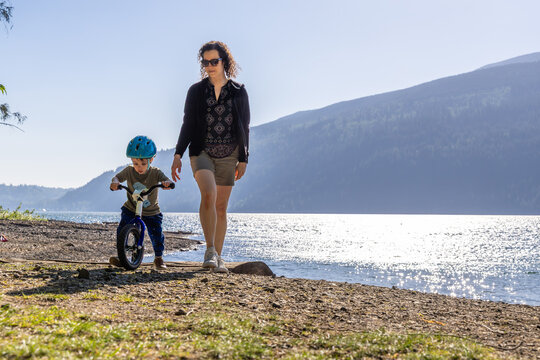Mother Teaching Son To Ride Balance Bike Along Cultus Lake Shore In Chilliwack, BC, Canada