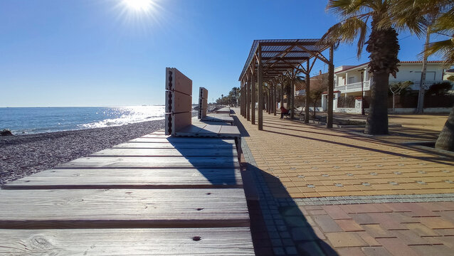 Wooden bench on a sunny boardwalk at Almenara beach Castellon