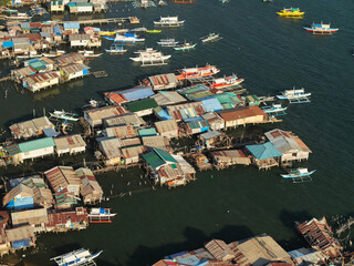 Aerial drone view of the floating fishing village in Coron, Palawan, Philippines. Traditional stilt houses, colorful rooftops, and Filipino outrigger boats line the coastal waters © akturer