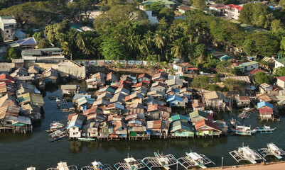 Aerial drone view of the floating fishing village in Coron, Palawan, Philippines. Traditional stilt houses, colorful rooftops, and Filipino outrigger boats line the coastal waters © akturer