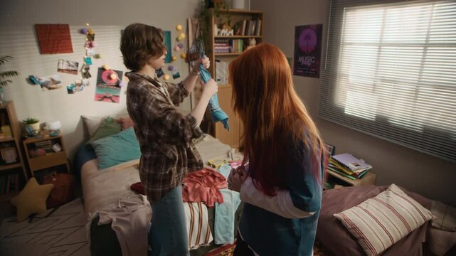 Eye level medium shot of two young Caucasian women trying humorous retro outfits and enjoying playful fashion moment in cozy bedroom