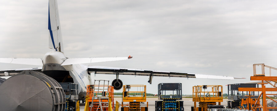 Cargo aircraft undergoing maintenance on airport apron hydraulic platforms service equipment cloudy sky. Industrial aviation scene engineering operations logistics support transport infrastructure