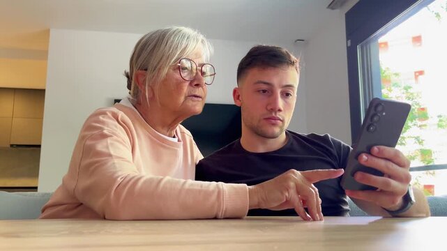 Grandson showing his grandmother how to use a smartphone, bridging the digital gap between generations.