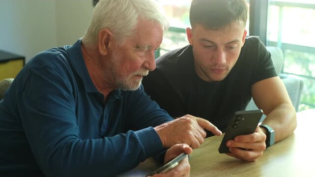 A young man teaches his senior father how to use a smartphone, bridging the generational gap through technology and shared learning at home.