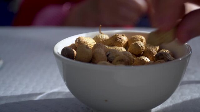 People pick up peanuts in their shells in a white bowl.