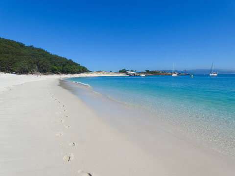 Wide view of Rodas Beach in the C&iacute;es Islands near Vigo, Galicia, with white sand, clear turquoise water, anchored sailboats and a bright blue summer sky