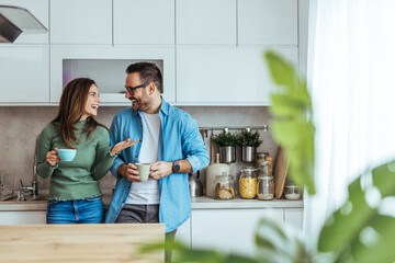 Obraz premium Happy Young Couple Chatting and Drinking Coffee in Bright Modern Kitchen Enjoying Cozy Morning Together