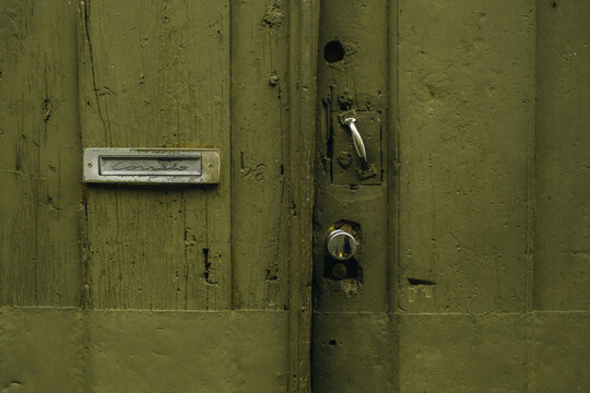 Close-up of a weathered olive green wooden door with vintage metal mail slot reading 