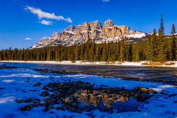 BANFF, ALBERTA, CANADA – Castle Mountain reflects in still waters in Banff National Park, its jagged snow-dusted peaks rising above dense coniferous forest in the Canadian Rockies. © ZOCC