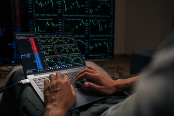Fototapeta premium Close-up cropped shot of investor typing on laptop with multiple financial and cryptocurrency charts on external screens, monitoring real-time market data for online trading and investment decisions.