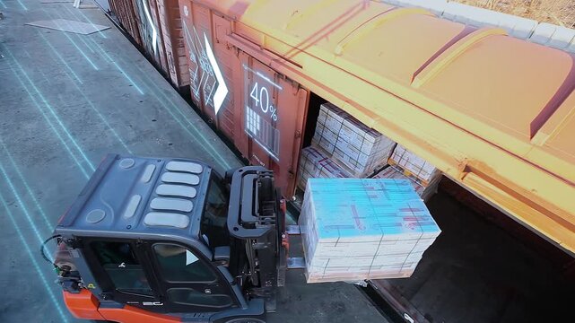 A forklift at the loading dock moves the products into the freight car. Smart logistics. Loading palletized products in cardboard boxes into a Boxcar. Concept of freight railroad transportation. Over 