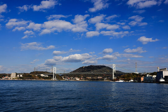 A large ocean liner departed, passing under Kanmon bridge toward the sea at Kitakyushu, Japan.