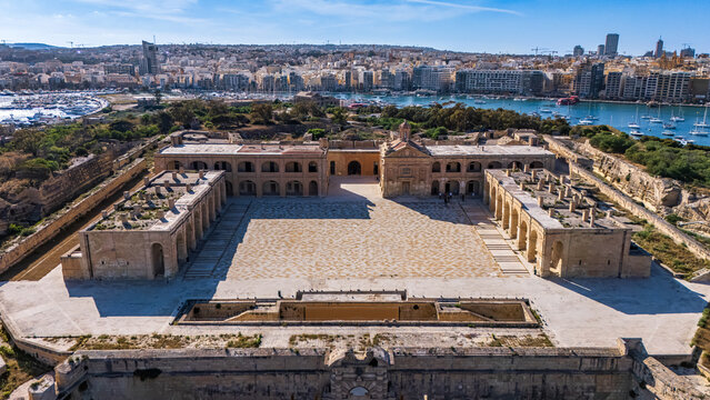 landscape low angle wide aerial drone shot of front of fort manoel on the outskirts of valletta malta with clear blue summer skies above with green trees surrounding and Mediterranean Sea water 