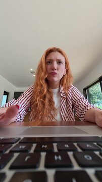 Stressed young woman with red hair feeling overwhelmed and frustrated while working on her laptop at home.