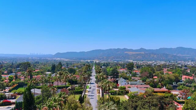 Highway lined up with the palm trees crosses the residential area. Hazy Hollywood Hills in Los Angeles, California, USA in the backdrop. Aerial view.