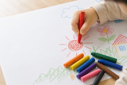 クレヨンで太陽と花を描く子供の手