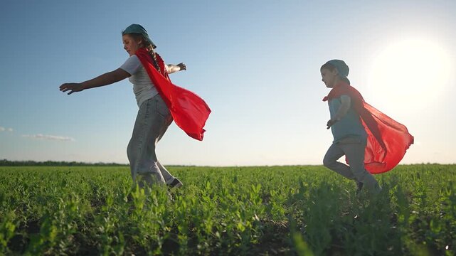 Boy chasing girl on green field. Kid wearing superhero cape laughing. Girl running playing with child on summer meadow. Boy enjoys superhero adventure. Running across field playing brings joy.