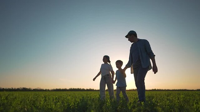 Father son daughter holding hands walk sunset field. Silhouette family together. Daughter laughs by father. Son holds hands tight. Family silhouette crosses field. Father daughter son happy together.