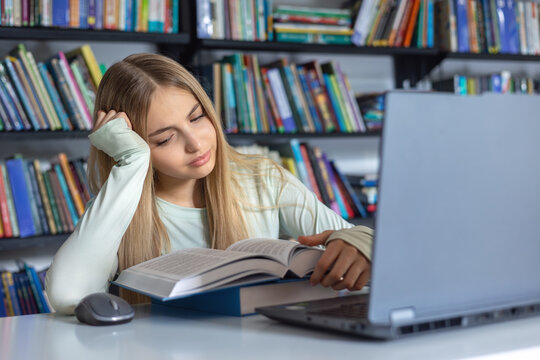 Teenage student feeling tired and unmotivated while studying in library, learning difficulties. Exhausted teen girl studying with books and laptop, academic fatigue and stress