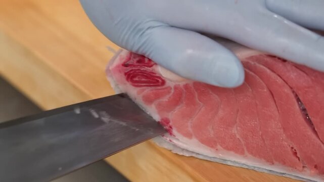 professional chef uses a sharp knife to masterfully slice a premium, bright red bluefin tuna loin on a wooden cutting board. This high-quality footage showcases the precision and art of Japanese culin