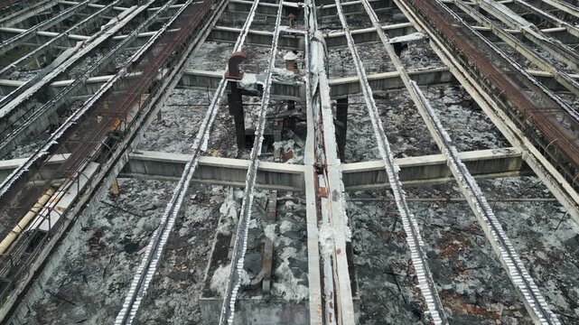 Aerial proximity shot of decaying industrial architecture revealing empty warehouse interior through rusty steel frame.