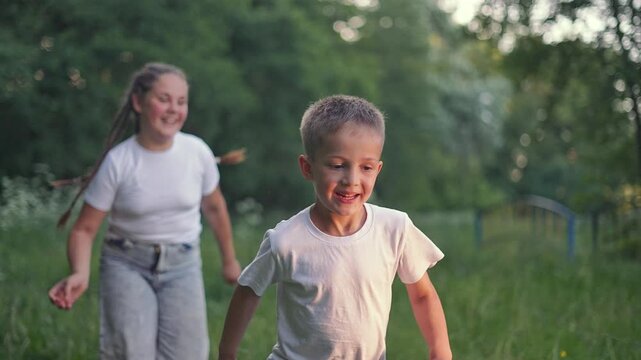 Boy running on green grass. Girl follows behind. Child plays fun outdoors game. Running child enjoys nature. Smile on boy face. Grass under feet. Children having fun running in outdoor game with smile