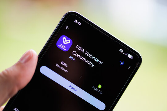 Close-up of a hand holding a smartphone displaying the FIFA Volunteer Community app on the Google Play Store