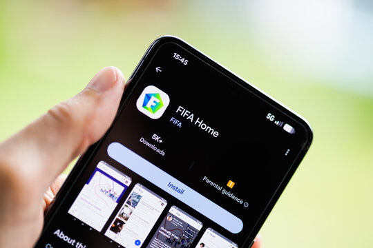Close-up of a hand holding a smartphone displaying the FIFA Home app on the Google Play Store