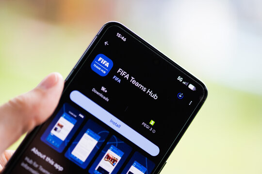 Close-up of a hand holding a smartphone displaying the FIFA Teams Hub app on the Google Play Store