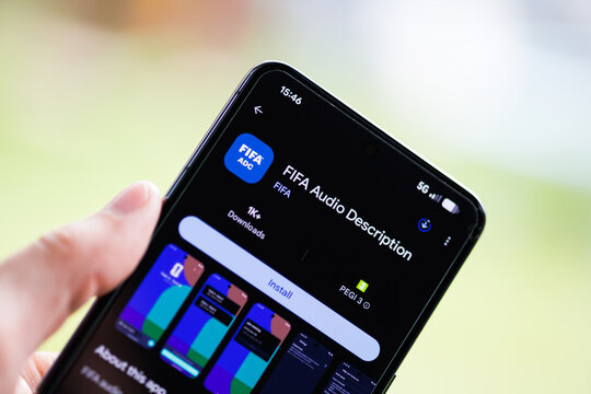 Close-up of a hand holding a smartphone displaying the FIFA Audio Description app on the Google Play Store