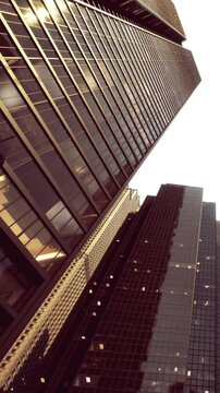Tall buildings stand close together in a city skyline as twilight approaches. Windows reflect light from their surroundings, showing a vibrant urban life.