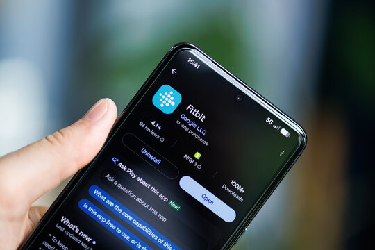 Close-up of a hand holding a smartphone displaying the Fitbit by Google LLC app on the Google Play Store