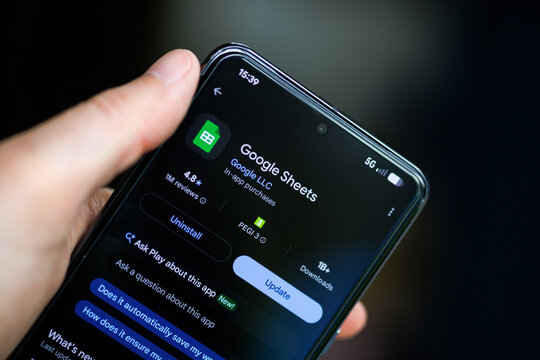 Close-up of a hand holding a smartphone displaying the Google Sheets app on the Google Play Store