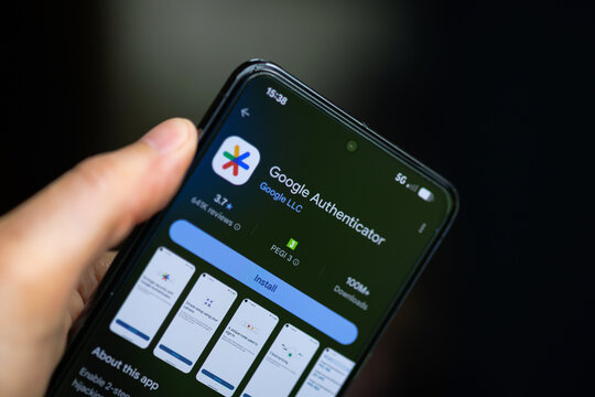 Close-up of a hand holding a smartphone displaying the Google Autheticator app on the Google Play Store