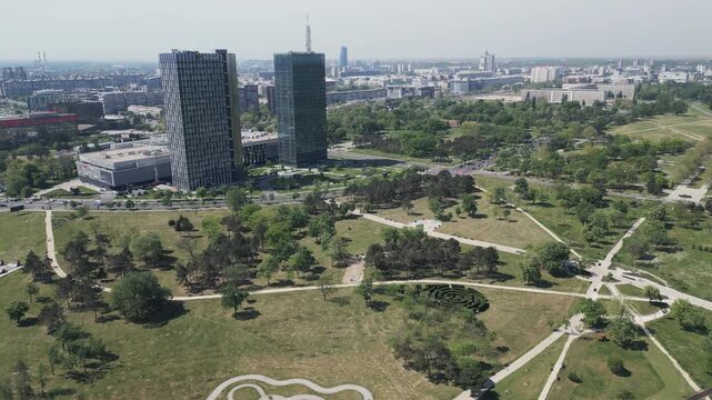 Wide panoramic drone view of lush green trees in Usce park with buildings and urban landscape behind, Belgrade Serbia.