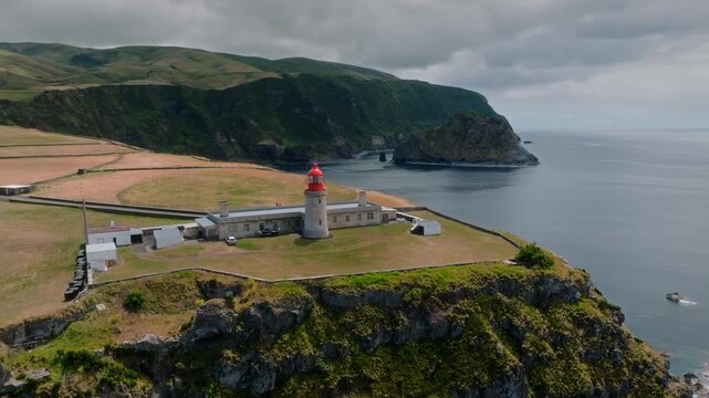 Epic Drone Orbit of Farol de Albarnaz Lighthouse on a Dramatic Rocky Headland with Craggy Volcanic Cliffs and Moody Skies, Flores Island