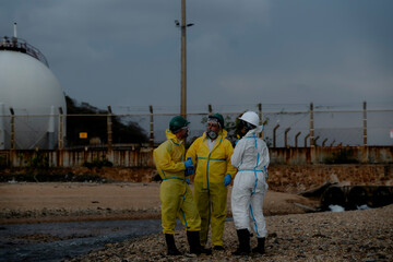 Fototapeta premium Environmental hazard and industrial pollution investigation concept. Hazmat team inspecting contaminated water near industrial gas storage facility and drainage canal