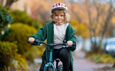Fototapeta premium Fall city scene with child on bike. Child rides bike on autumn. Safe kid cycling on street. Happy child learning to bike ride. Child with bicycle in autumn fall park.
