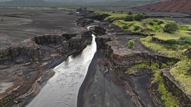 Volcanic river flowing through deep canyon carved into erosion resistant lava rock, showcasing rugged coastline and unique geological formations. Port Resolution, Tanna Island. Aerial view drone shot