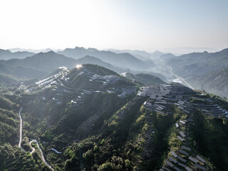 Fototapeta premium Terraced fields and village nestled in green mountains under bright sunlight