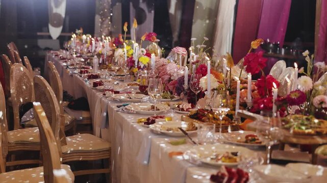 Banquet table setting with elegant chairs, beautiful flowers and burning candles for wedding reception in 4k slow motion. Luxury dinner event decoration layout, festive anniversary venue interior.