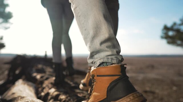 Adventurer's brown hiking boot steps carefully along weathered fallen tree trunk during wilderness trek. Rugged outdoor footwear navigates natural obstacle on sunny forest trail expedition.