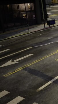 Street scene shows traffic signs and markings on the road at night. The area appears empty with a few signs visible and dim lighting from nearby buildings.