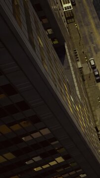Cars are parked along the side of a city street at night. Streetlights cast light on the asphalt. Tall buildings surround the area. Few people are walking in the distance.