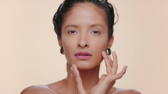 Close-up shot of south american woman with caramel toned skin strokes her face evoking matte skin over beige background | Beauty commercial concept