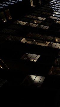 Tall building with many glass windows reflecting lights. The scene shows a view from below looking up at the building. The time is evening as light fades in the sky.