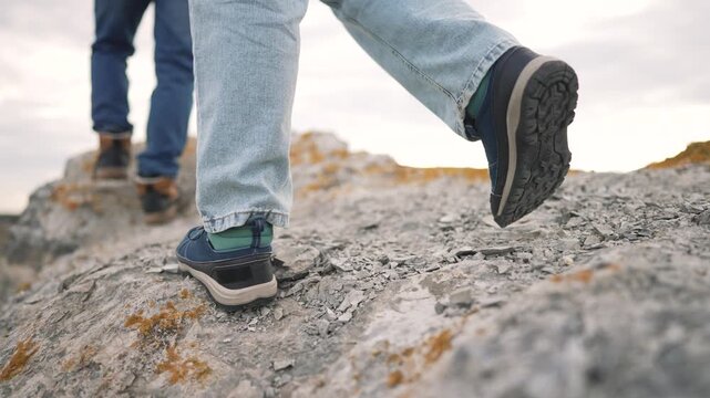 Hiker stepping carefully on rugged rocky terrain wearing sturdy hiking boots with green accents. Person navigating challenging mountain trail covered with lichen during outdoor trekking adventure.