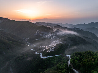Fototapeta premium Aerial view of rural terraces and winding road surrounded by mountains with mist at sunrise
