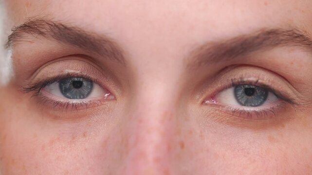 Extreme close up of Latina with light complexion and blue eyes opens eyes and looks at camera on tan background | Beauty care advertisement