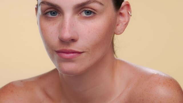 BCU shot of light-complexioned Latina with freckles gently strokes her shoulder evoking balanced skin on beige bg | Beauty care advertising concept